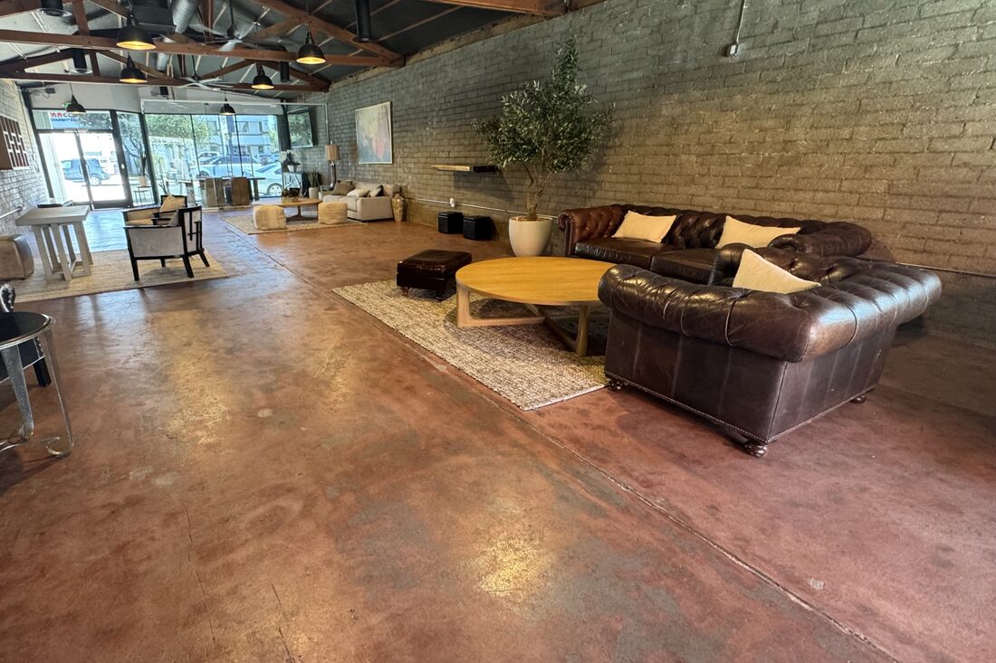 Leather chesterfield sofas and round oak table with a potted olive tree against the brick wall, entry glass beyond
